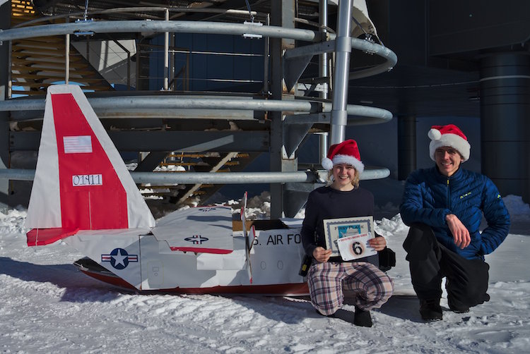 Two people posing with cardboard sled of plane