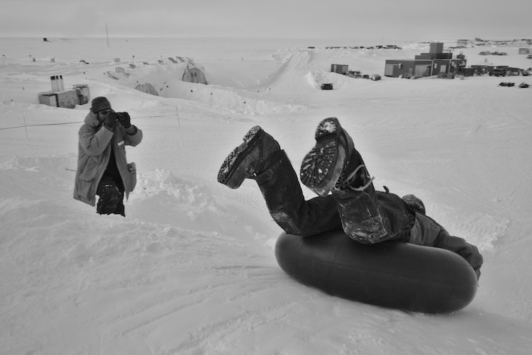 Black and white photo of person about to sled down hil head first on a tube