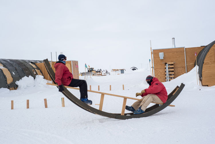 Side view of two people on a makeshift seesaw out on the snow.