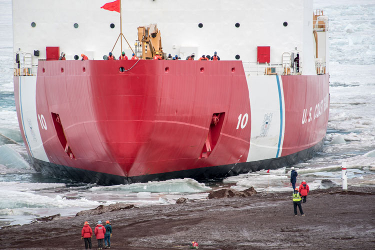 Close up view of bow of icebreaker ship, with people visible on board and on shore