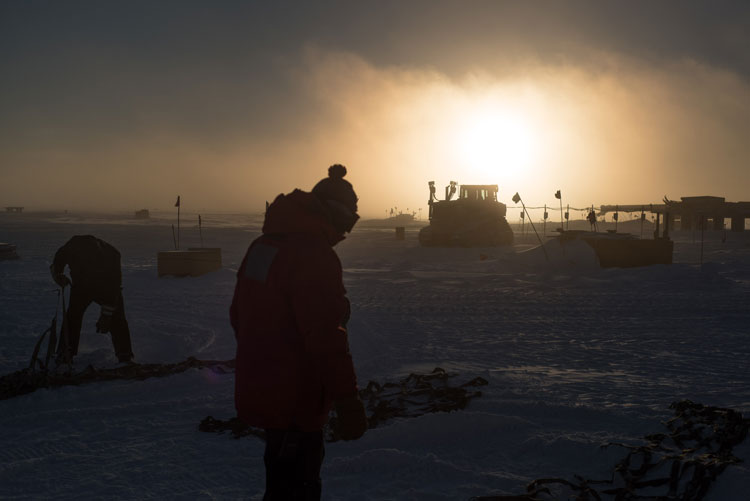 Shadowed figures in foreground, sun low on horizon