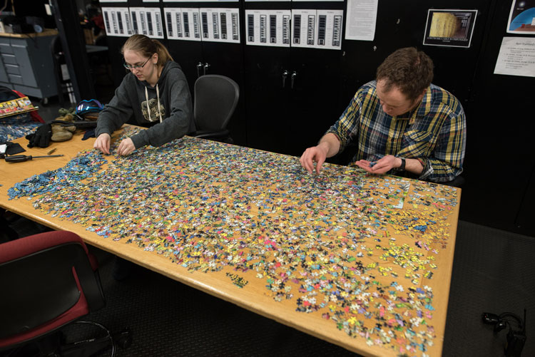 Two people at long table working a jigsaw puzzle