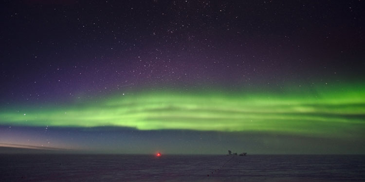 Bright horizontal band of auroras, with lingering light from sunset along horizon, starry sky above