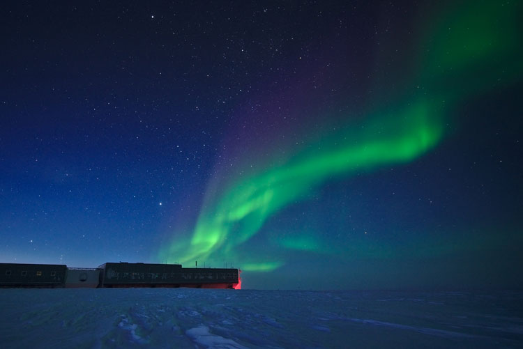 Slender green aurora in bluish sky above South Pole station