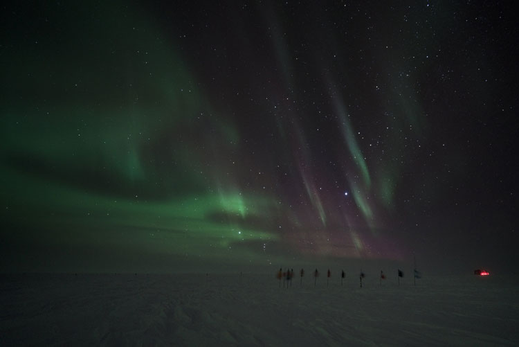 Aurora shower over flags at ceremonial South Pole