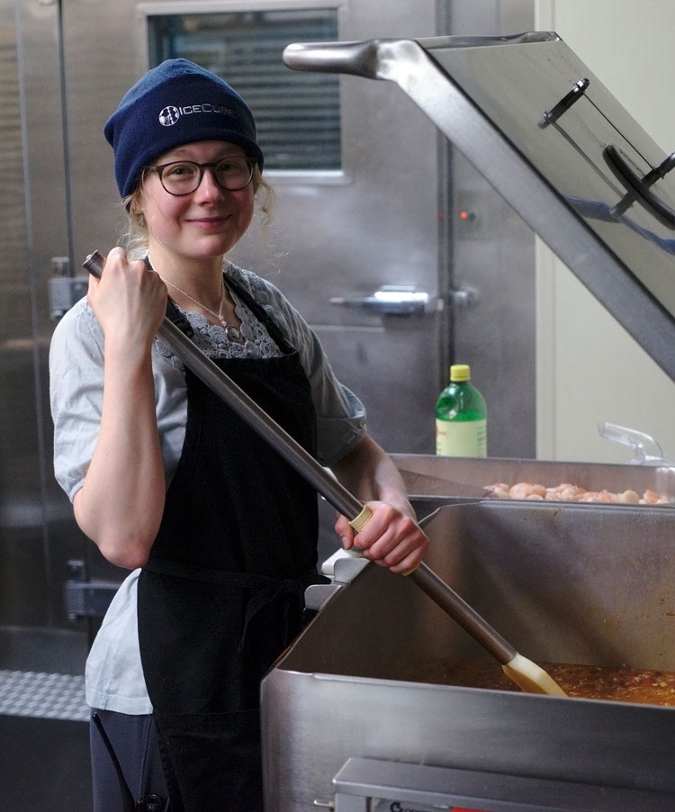 Winterover smiling, stirring large vat of paella.