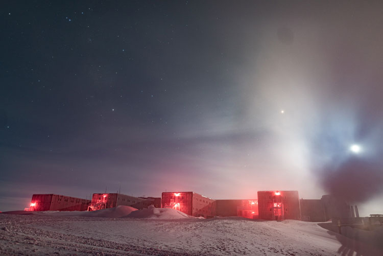 Bright moon in blue sky above South Pole station, lit in read/