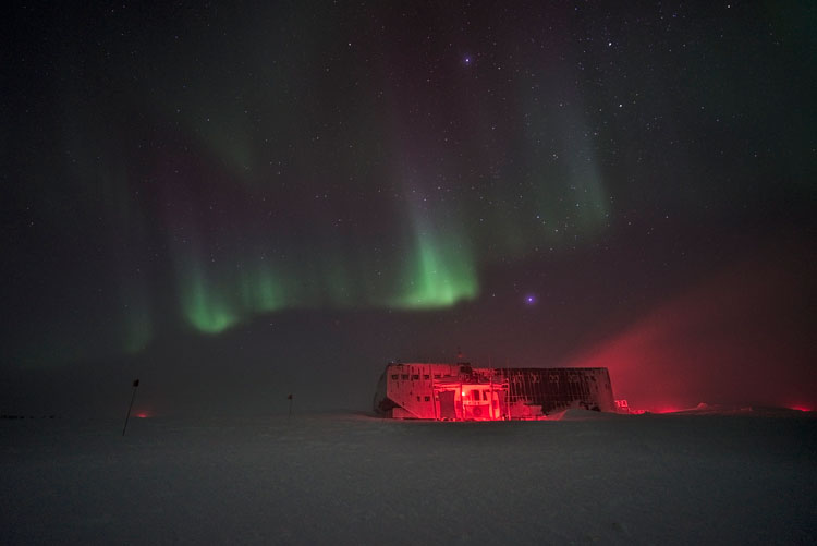 Green auroras in sky over South Pole station lit up in red