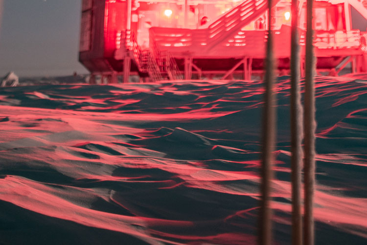 Red-lit image of IceCube Lab, blurry in background, with foreground of snow surface appearing as choppy waves