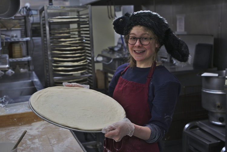 Person holding round pizza pan covered in unbaked dough