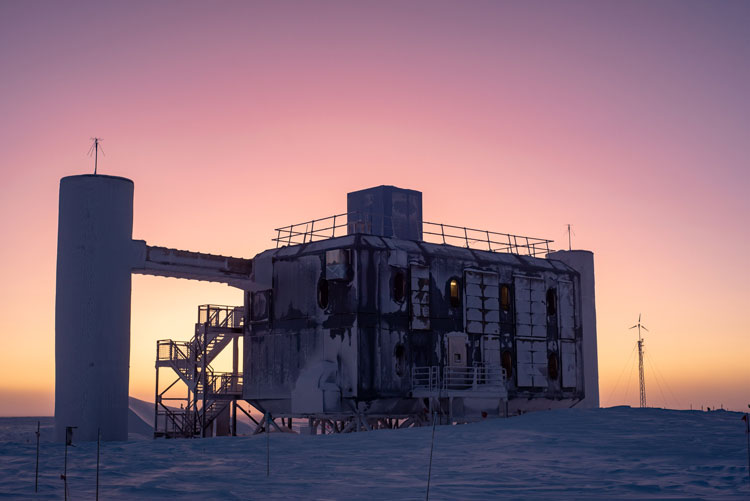 Frosty IceCube Lab in shadow, with colorful sky at sunrise in background.