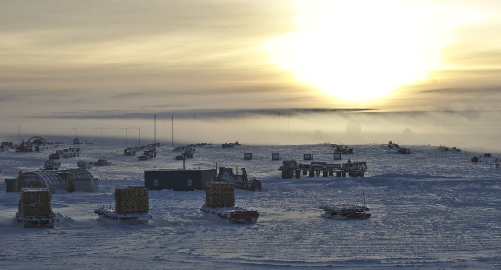 Sun low in sky at South Pole, equipment on ground in groups