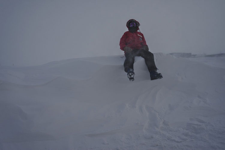 Person sitting on top of tall snow drift