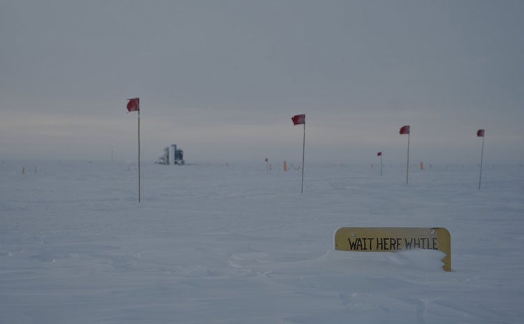 Outside at South Pole, line of flag markers and snowed-in sign on ground