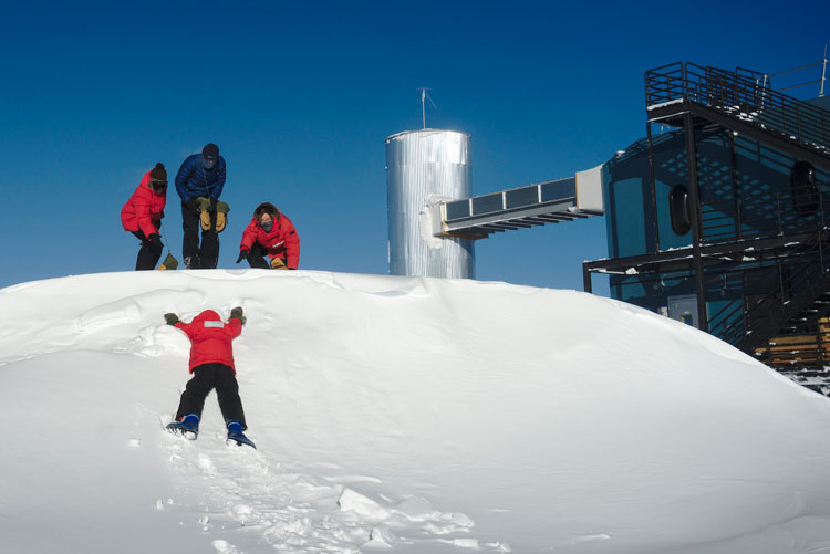 four people in parkas on snowdrift, three standing on lying down