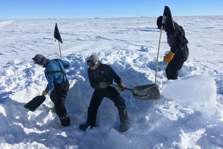 Three people digging in snow at South Pole