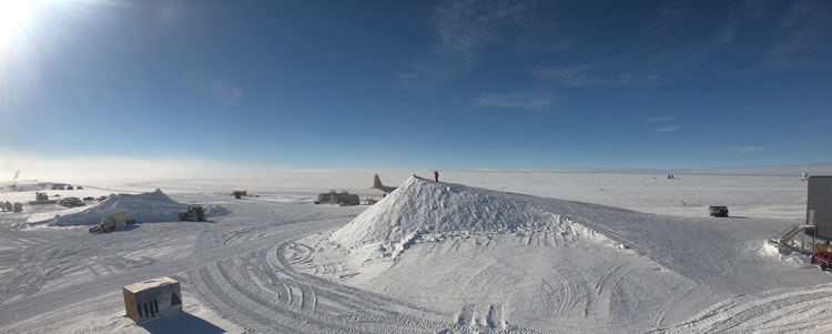 Person, tiny in distance, standing on top of giant snow hill, with view all around of south pole