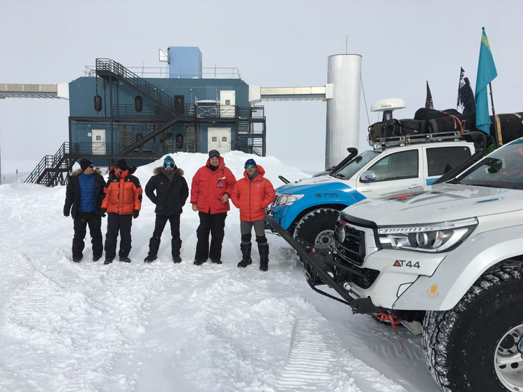 Five people in front of ICL, facing camera, standing next to two large arctic vehicles