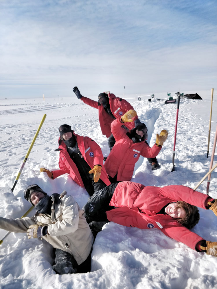 Five people with arms raised, standing in freshly dug trench at the South Pole