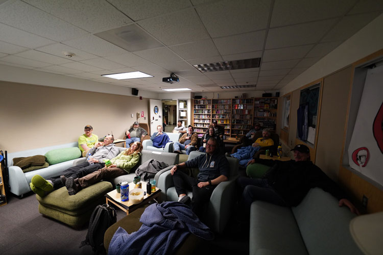 South Pole station TV room, group relaxing on sofas and chairs watching show together