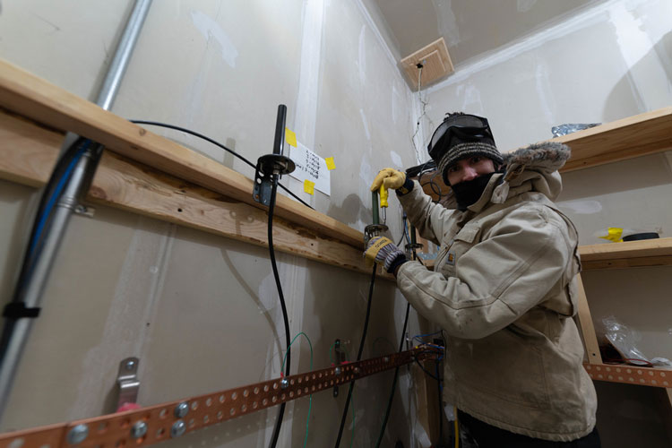 Person wearing parka indoors, working with cable and screwdriver
