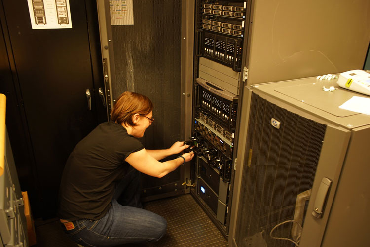 Person crouching in front of rack of computers