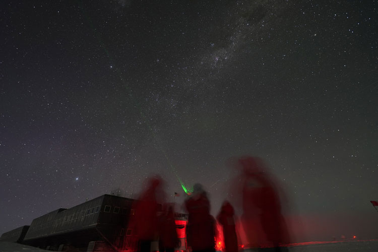 People burry in foreground pointing with laser up at starry sky