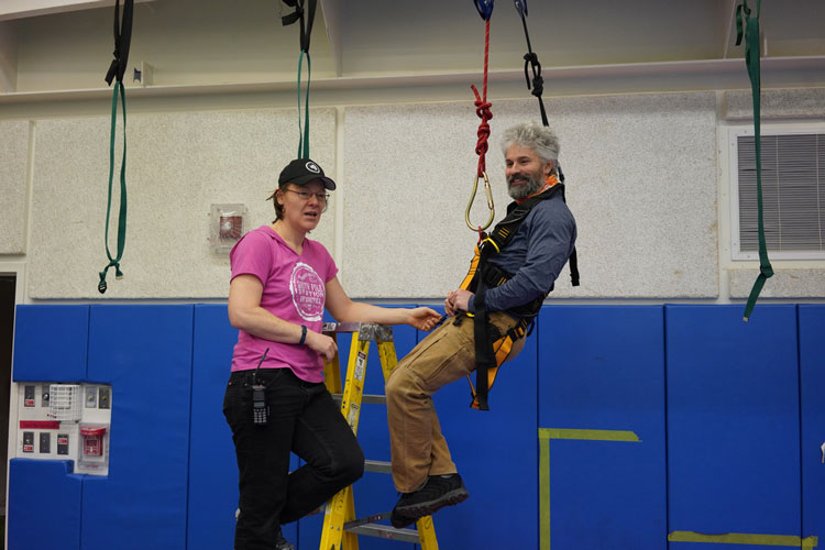 Two people in gym, one in harness