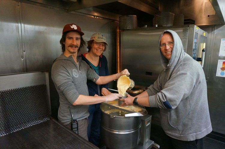 Three people cooking around a big pot