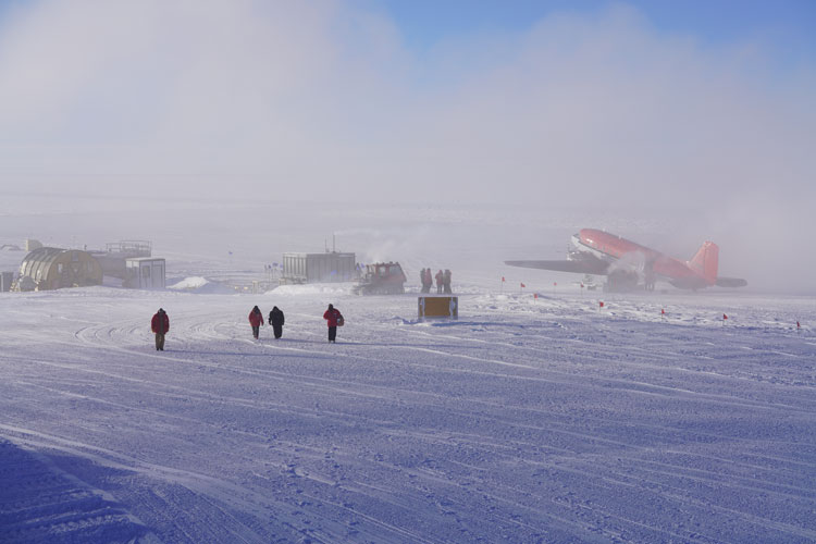 Red parkas walking on snow, parked plane