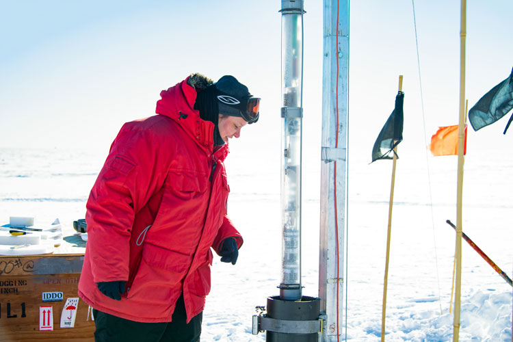 Person in red parka looking down into an ice coring apparatus