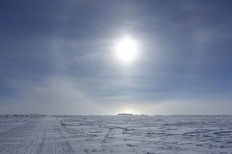 South Pole station in distance on horizon, bright sun with halo overhead