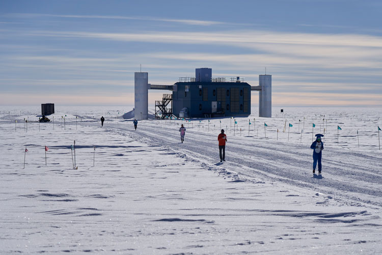 View of some racers along a path at the South Pole, with the IceCube Lab to the right