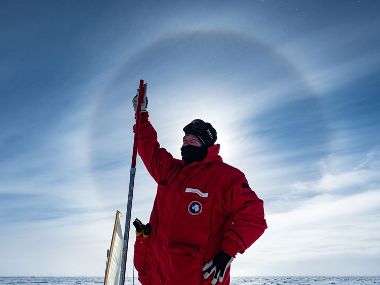 Person in red parka with head centered on sun halo in sky