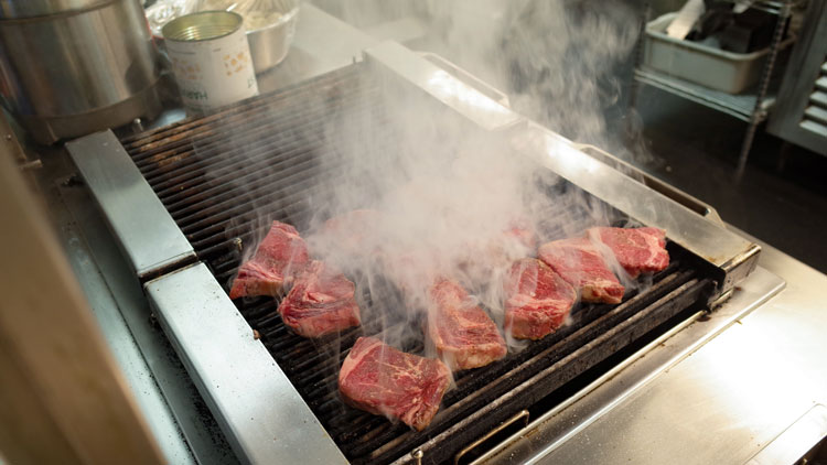 Smoke rising from steaks on indoor grill.