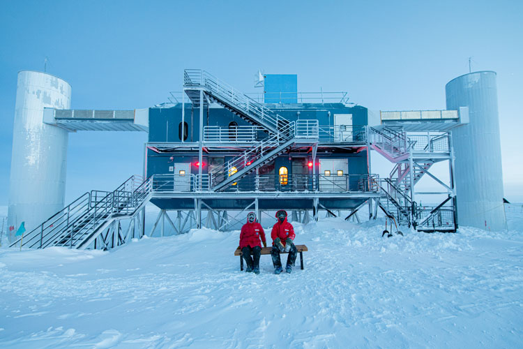 Twilight shot of IceCube Lab, with winterovers outside in front, seated on a bench facing camera