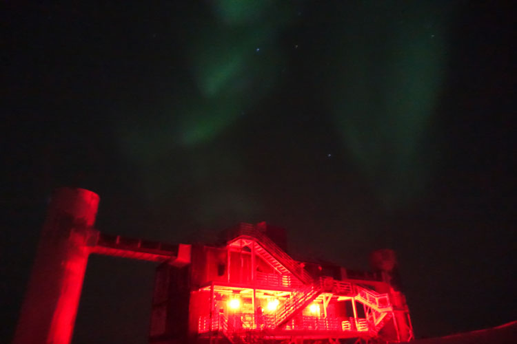 IceCube Lab lit up in red, faint wisps of aurora overhead