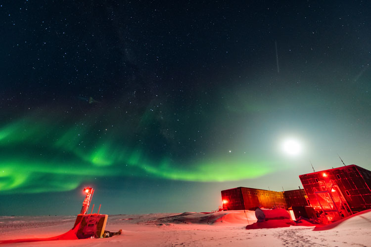 South Pole station, lit in red, under bright moon with some auroras