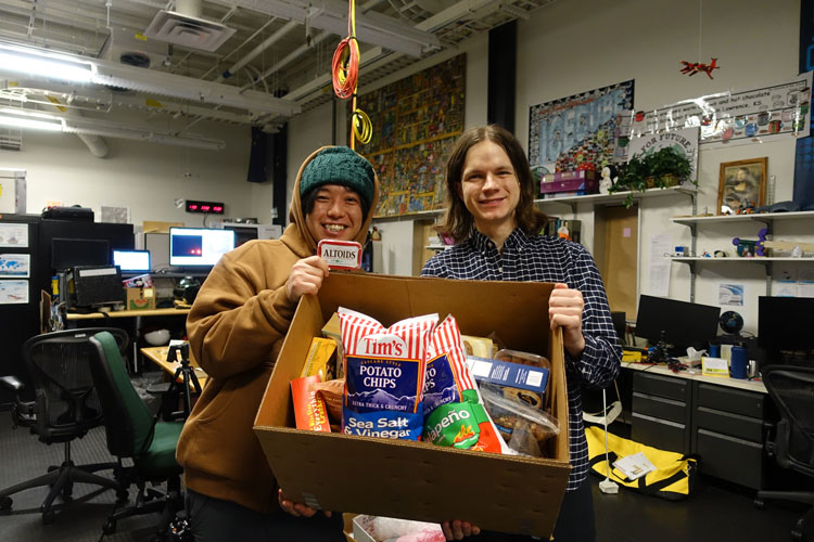 Two people holding open a big box full of snack food