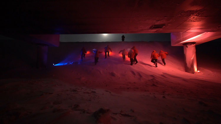 Dark outside, lit in red, group of people climbing a snow bank under station