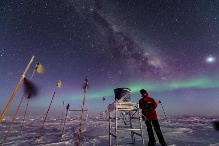 Person working outside in red parka, starry sky with Milky Way and aurora visible