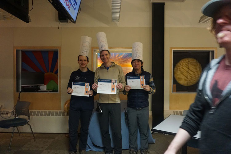 Three individuals donning paper toques as winning Iron Chef team