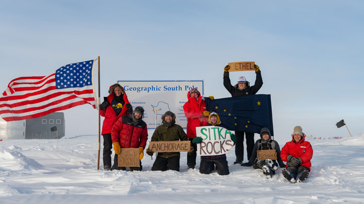 Group photo of eight, at the geographic South Pole sign