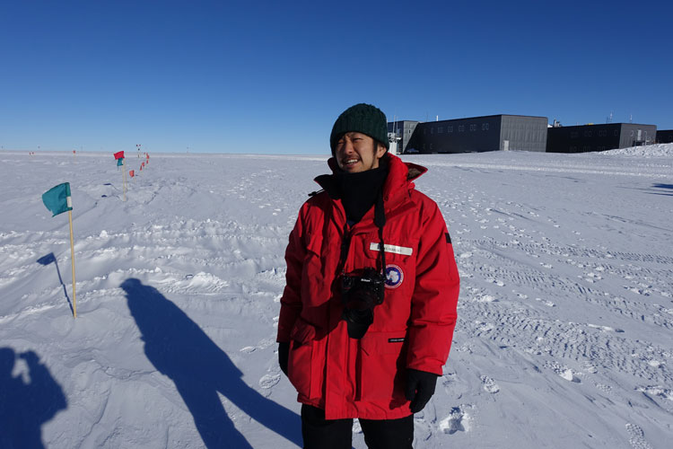 Person standing in red parka, looking at sky awaiting a flight arrival