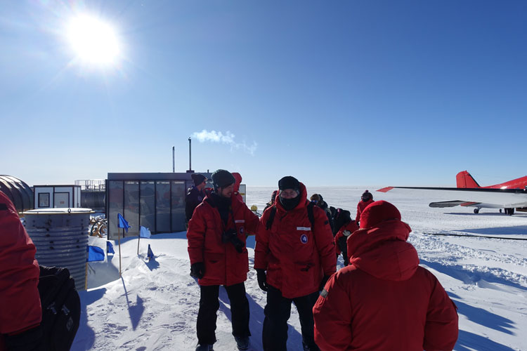 Group of people in parkas, plane on ice in the background