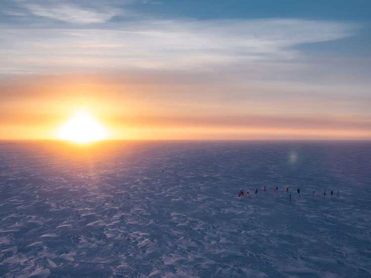 Bright sun on horizon, highlighting texture of the icy surface.