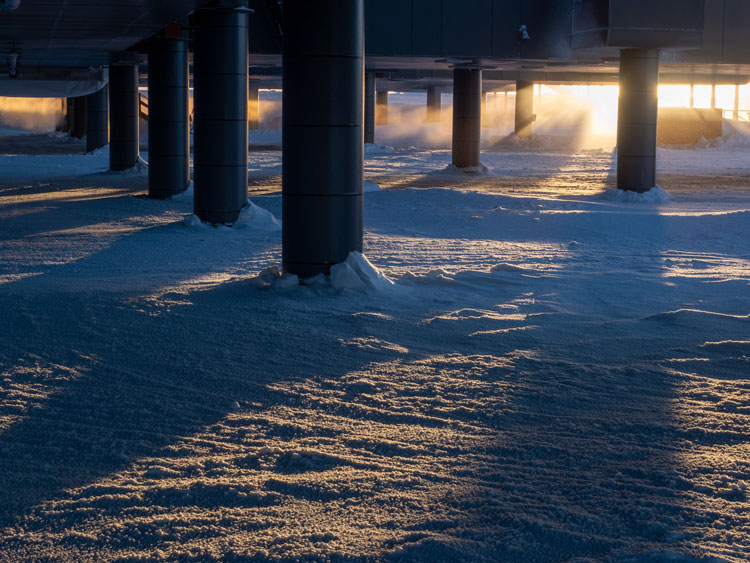 Sunlight casting shadows from behind dark columns below South Pole station.