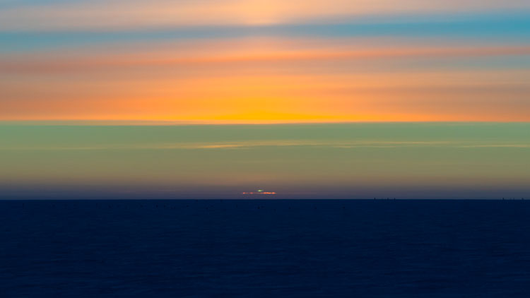 : Sun’s green flash visible at sunset, with colorful cloud-filled sky.