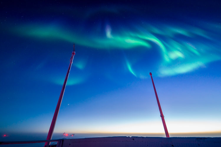 Swirling green auroras against blue sky, from observation deck of South Pole station.