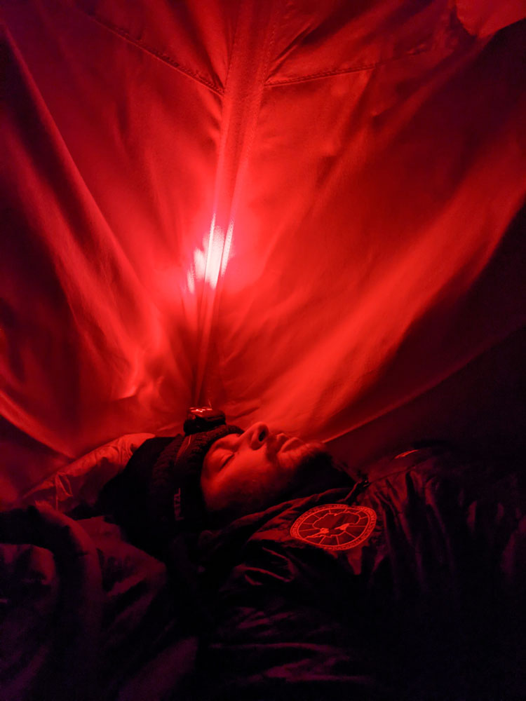 Individual sleeping inside tent, lit in red light.